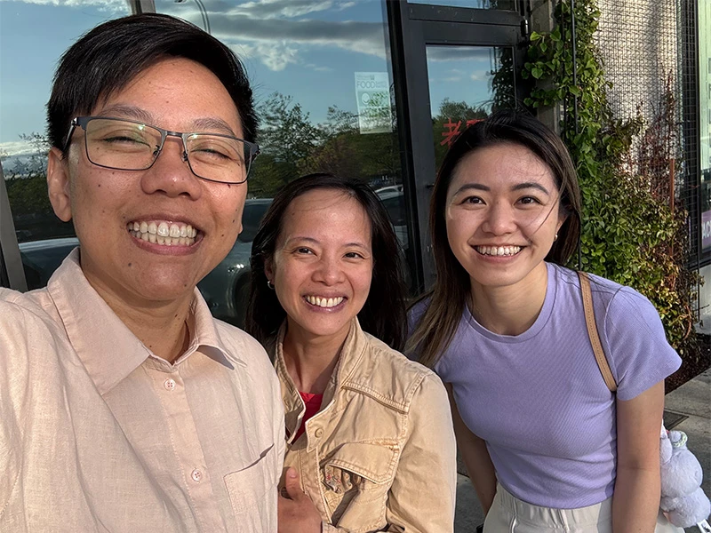 Three smiling dentist standing close together outdoors, taking a casual group selfie in front of a building